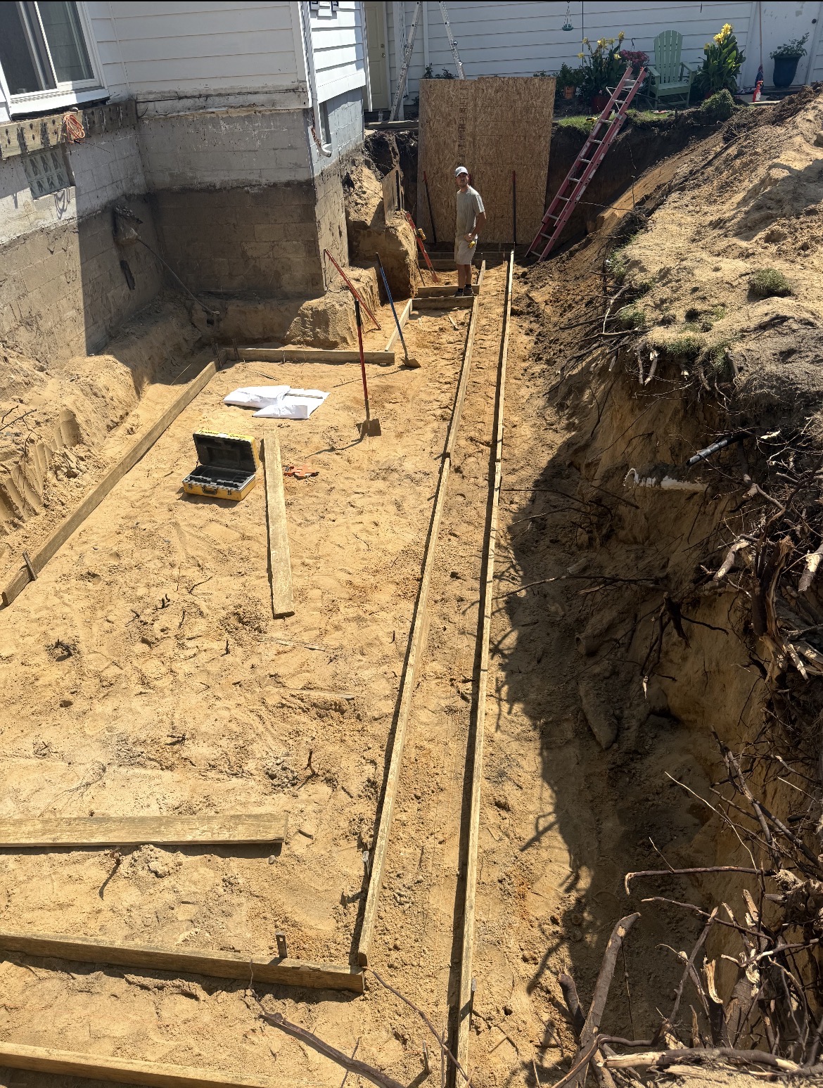 Footing forms set in a hand-dug basement excavation beside a home